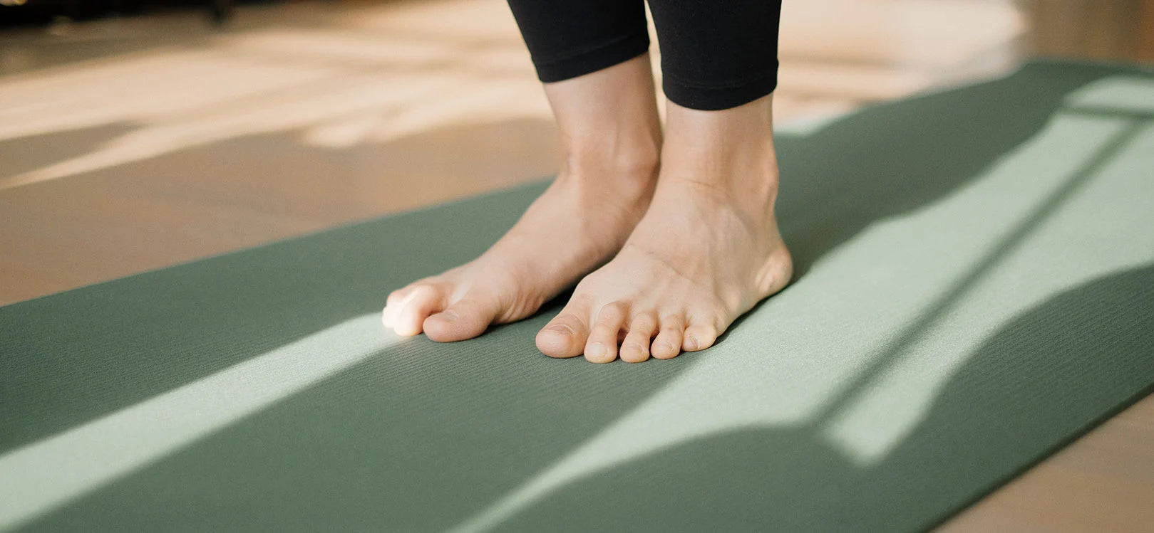 Person's feet standing in centre of sage green pilates mat